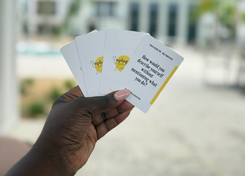 Hand holding three cards with text and a logo against a blurred outdoor background

